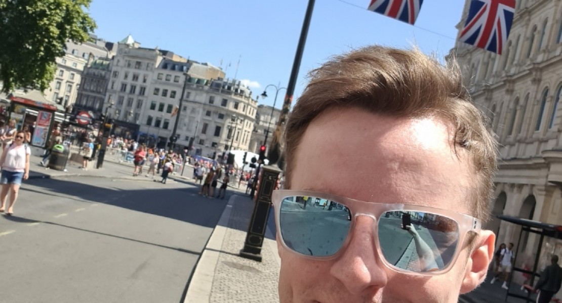 A picture of myself (Luc Shelton) posing with my medal after running the ASICS London 10K. Behind me is a string of Union Jack flags hanging across the street next to Trafalgar Square.