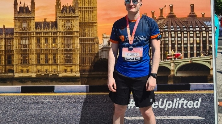 A picture of myself (Luc Shelton) posing with my medal after running the ASICS London 10K. I'm standing in front of a photo backdrop.